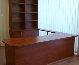 Compact dark wooden reception desk with rear shelving and cabinets beside a window with white blinds.