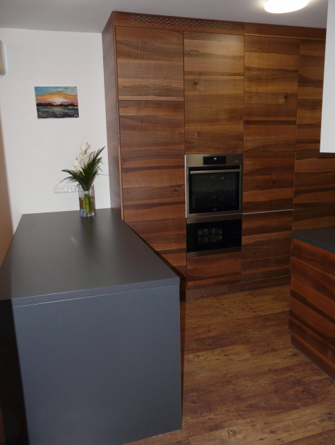 Wood-grain kitchen with tall appliance cabinets, dark gray counter, openwork trim, and wood-look flooring.