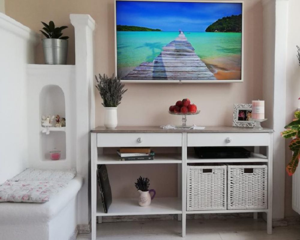 White living-room media console with open shelves, wicker baskets, decorations, and a wall-mounted television.