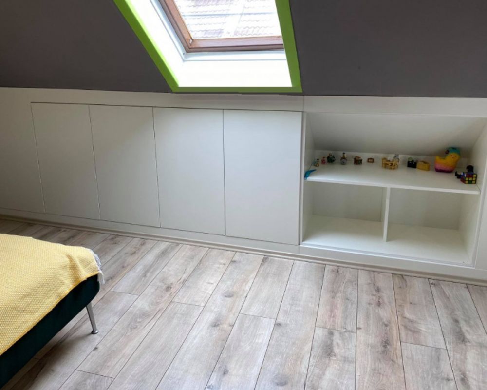 White attic built-in cabinets with handleless doors, toy display shelves, and a green-framed roof window.