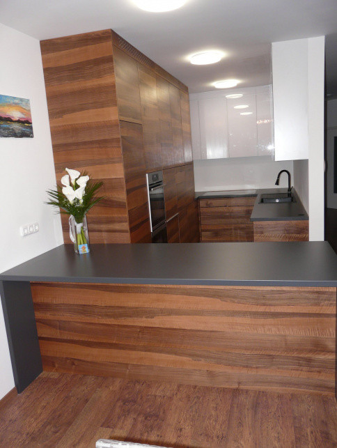 Modern wood-grain kitchen with a large dark island, built-in oven, sink, and glossy white upper cabinets.