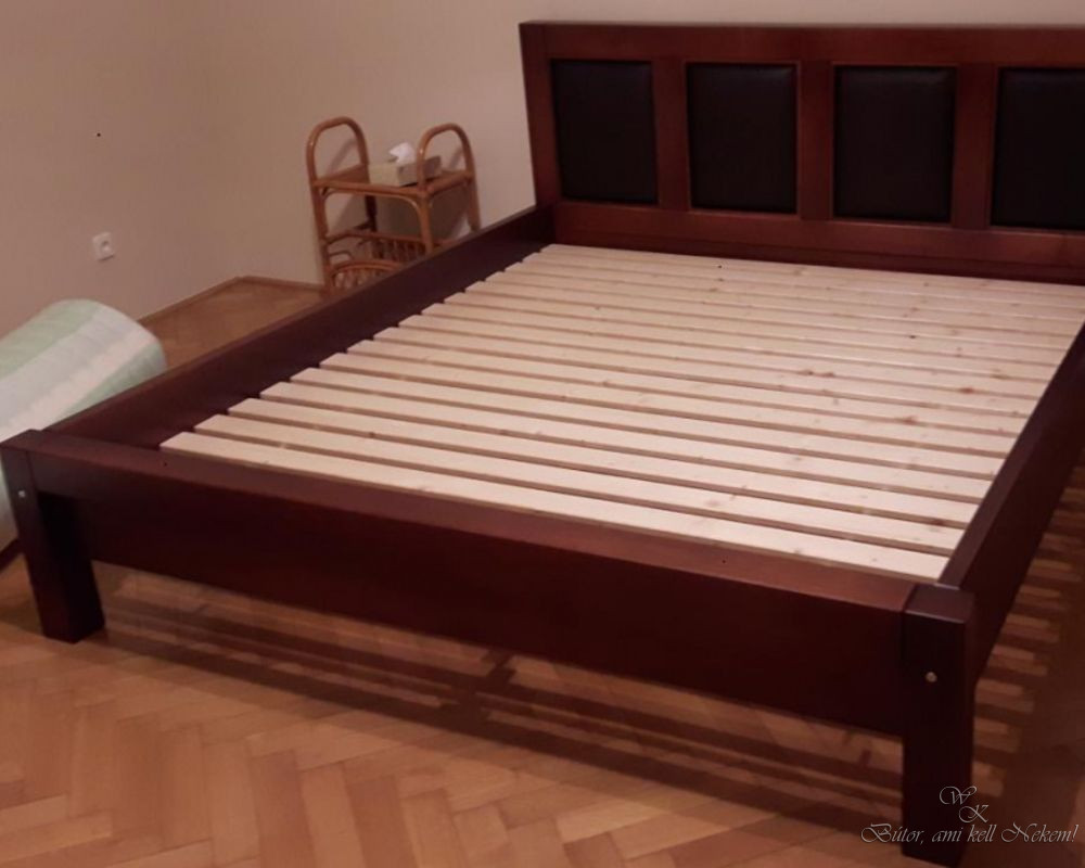 Dark wooden bed frame with a four-panel headboard and exposed wooden slats in a bedroom.