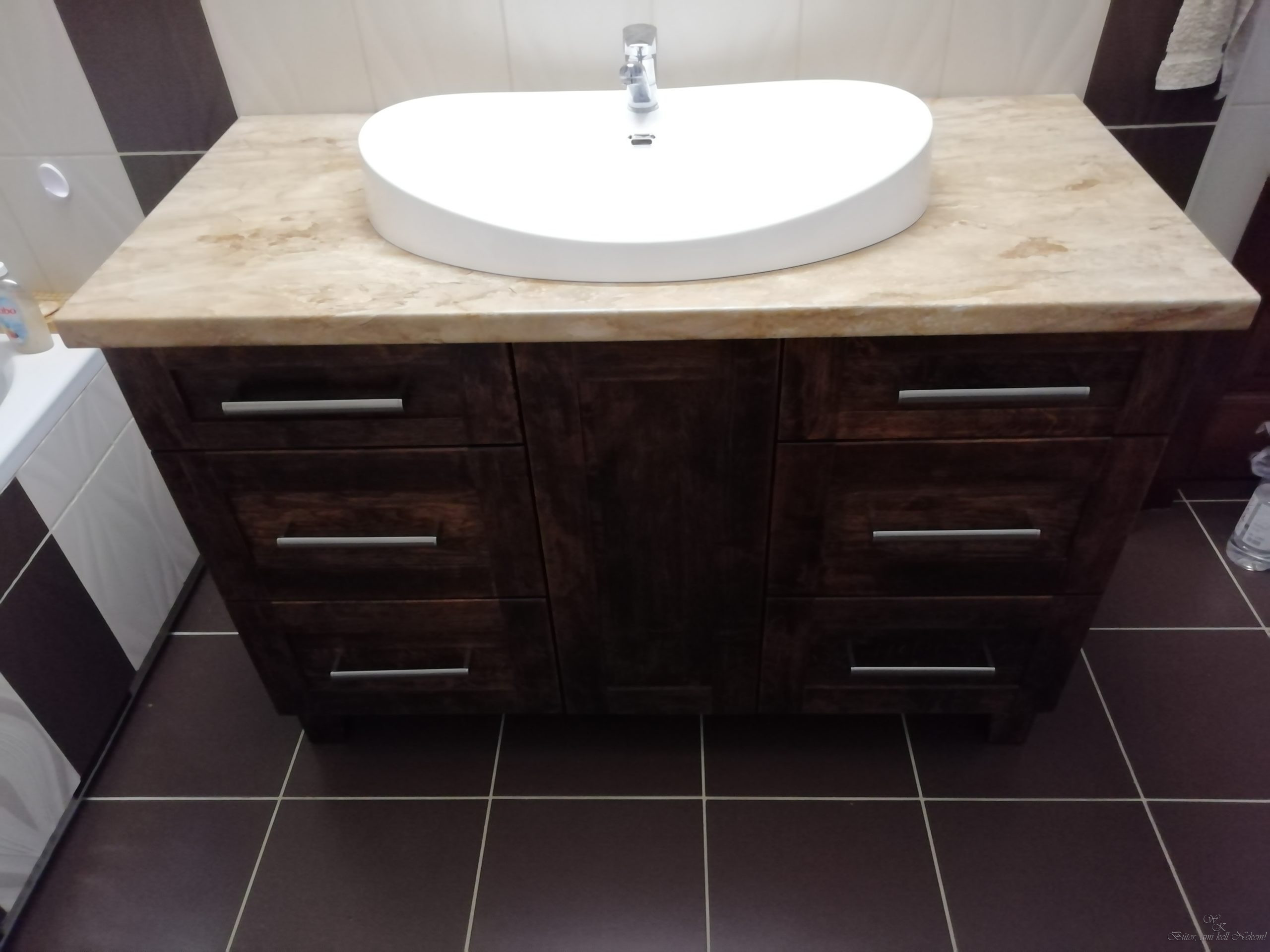 Dark wood bathroom vanity with white oval basin, chrome faucet, drawers, and dark tiled floor.