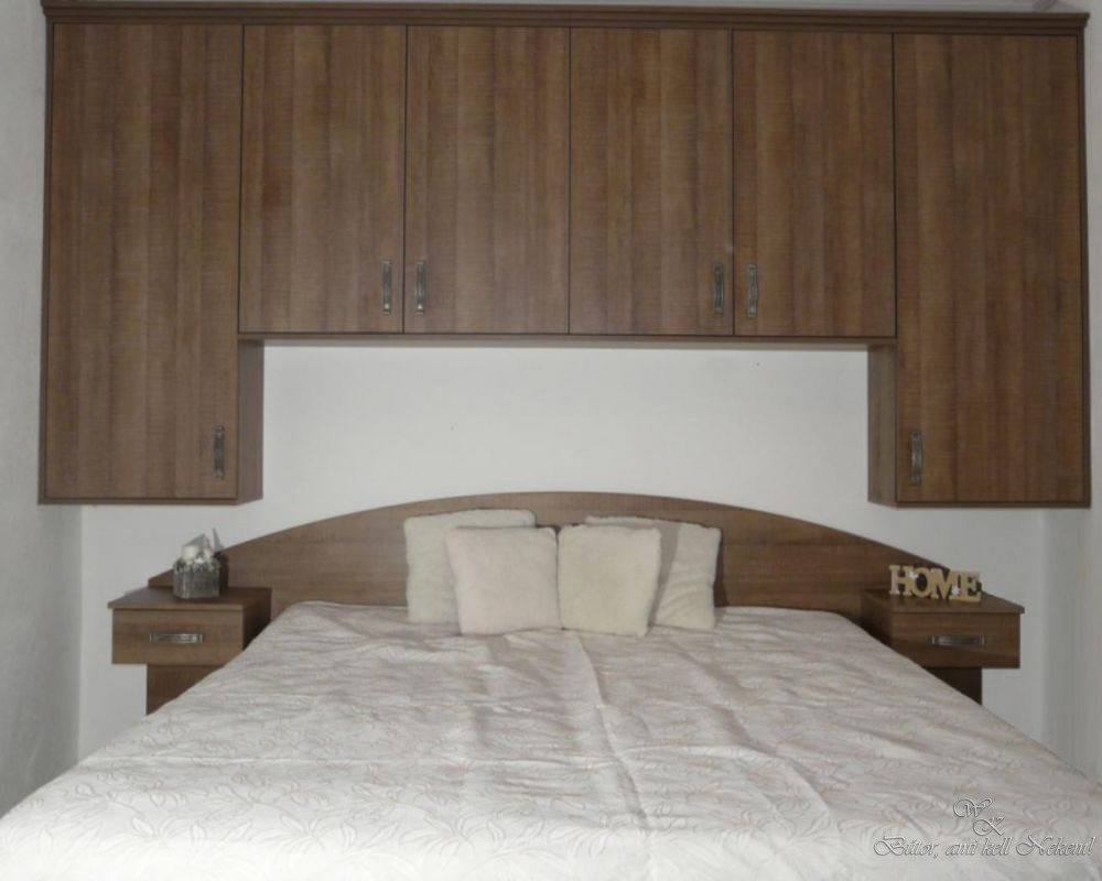 Dark wood bedroom wall unit with overhead cabinets, curved bed headboard, bedside tables, and a made bed.