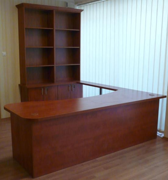 Dark wood L-shaped reception desk with rounded corner, rear shelving, lower cabinets, and window blinds.