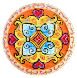 A circular ornamental design fills the image against a white background. Red hearts, pale blue curls, orange petals, and a central red diamond form a symmetrical pattern. A peach-colored border surrounds the motif.