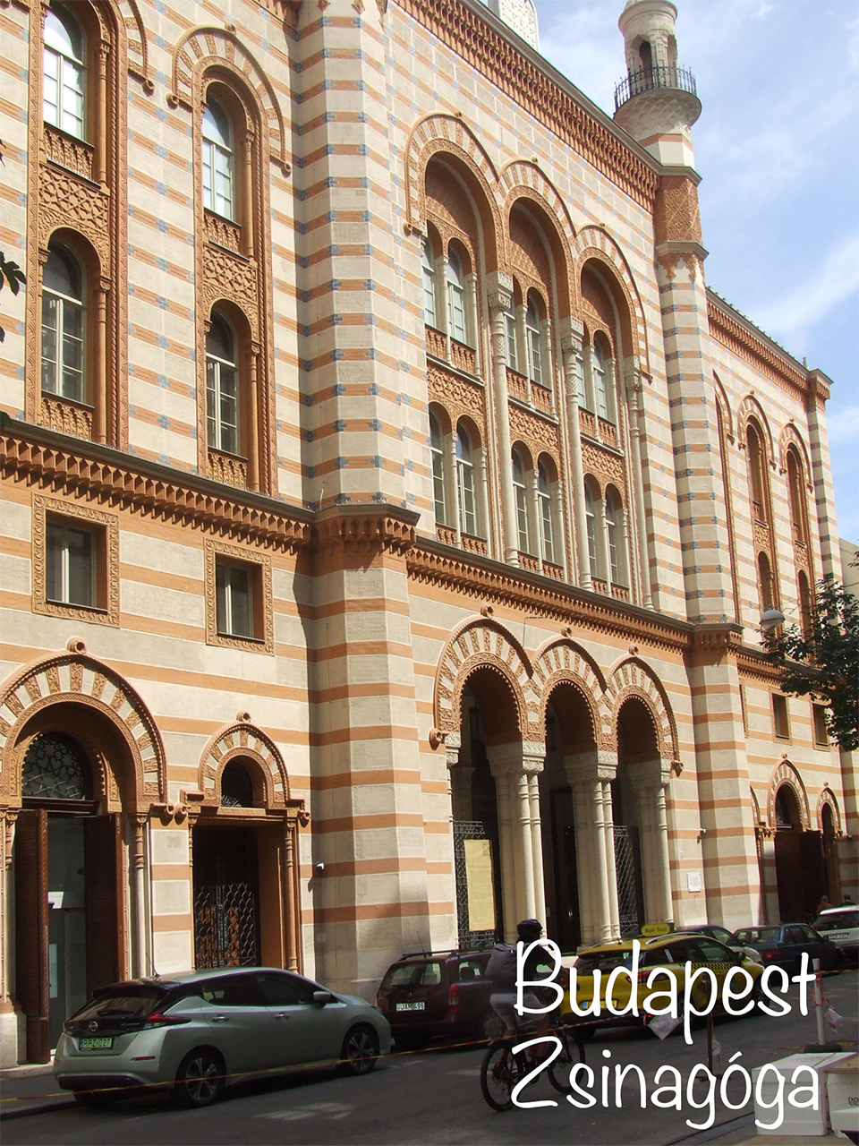 Ornate striped facade of Budapest's Rumbach Street Synagogue beside a city street.