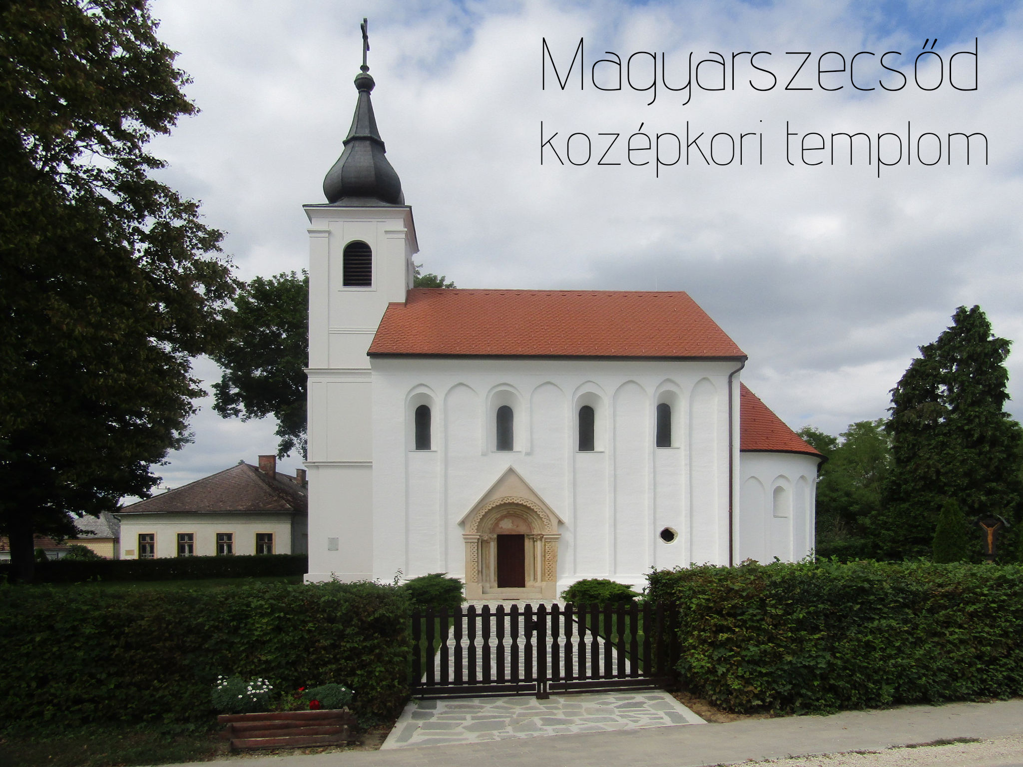 White Magyarszecsőd medieval church with dark spire, red roof, and carved entrance.