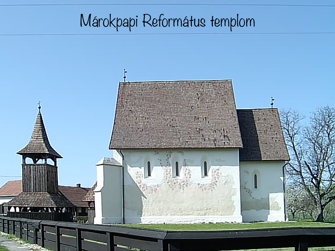 Márkopapi Reformed Church and its timber bell tower behind a dark fence.