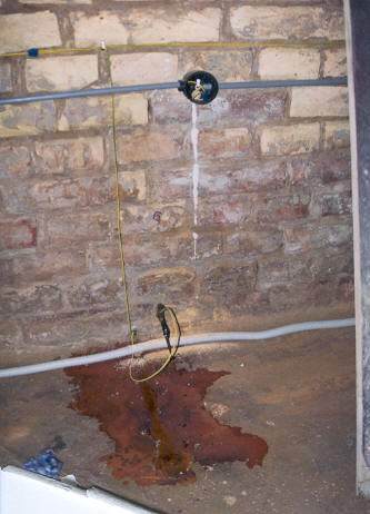 Exposed brick wall with cables and a dark damp stain spreading across the floor.