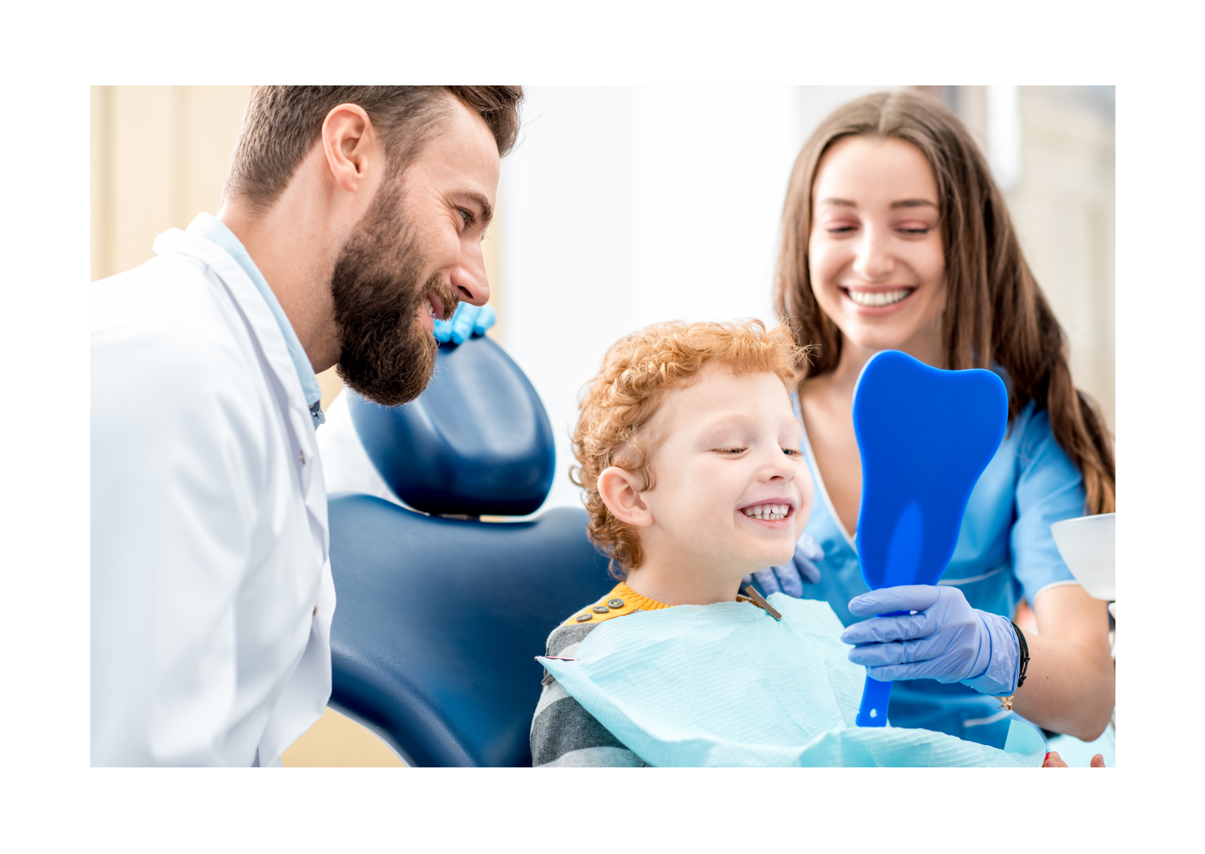 A bright dental-room scene appears inset within a wide white border. A child reclines in a dark blue chair while a bearded adult in a white coat leans in from the left and a smiling adult in blue holds up a blue heart-shaped mirror at the right. The child wears a pale bib, and no readable text appears.