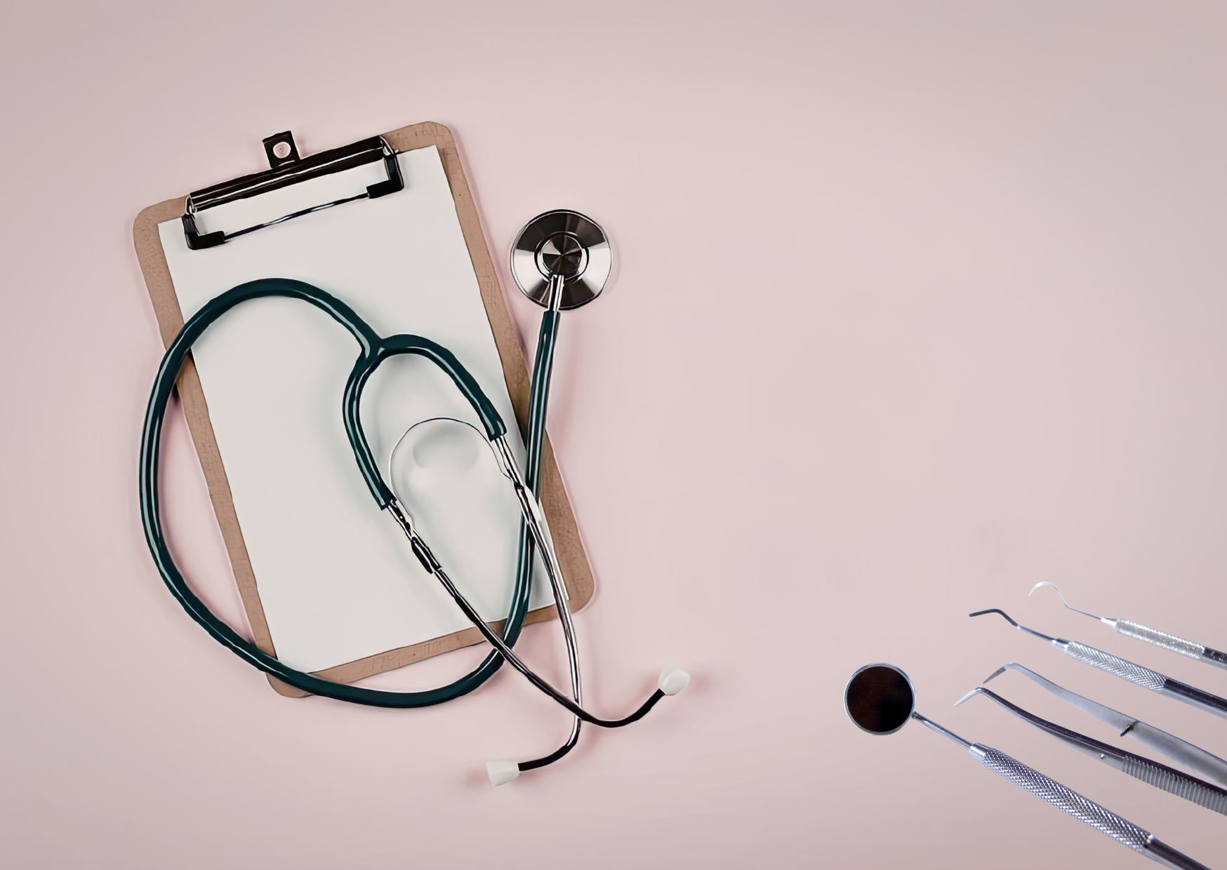 A dark stethoscope is draped over a blank white sheet clipped to a brown board on a pale pink surface. Several shiny metal dental instruments extend into the lower-right corner, including a round mirror and narrow curved tools. The objects are arranged diagonally with ample open pink space at the right, and no legible text appears.
