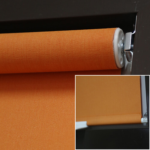A close-up shows orange textured fabric wrapped around a cylindrical roller mounted inside a dark window frame. The white circular roller end cap and adjacent bracket are visible at the upper right. A small inset image at the lower right shows another view of the orange shade near the window frame. The composition focuses on the mechanism and woven-looking surface.