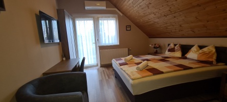 Tetőtéri hálószoba mintás ágytakaróval, fotellel és ablak melletti asztallal.