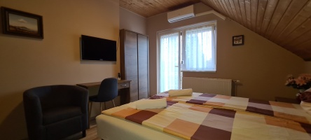 Tetőtéri szoba étkezőasztallal, fotellel és ablakkal a ferde fa mennyezet alatt.