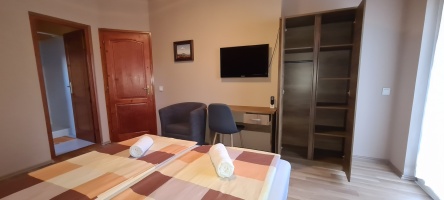 Tetőtéri szoba étkezőasztallal, két székkel, fotellel és fali televízióval.