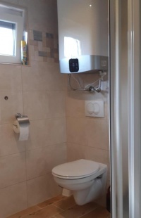 Fali WC és fehér vízmelegítő ablakkal a csempézett fürdőszobában.