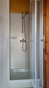 Fehér csempés fürdőszobai zuhanykabin kézi zuhanyfejjel.