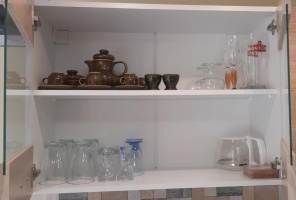 Üvegpoharak, kancsók és kerámiakannák nyitott szekrényben.