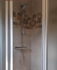 Krómozott zuhanypanel és kézi zuhanyfej a csempézett zuhanyfülkében.