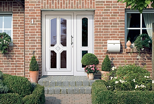 Brick house entrance with a decorative white glazed door and planted steps.