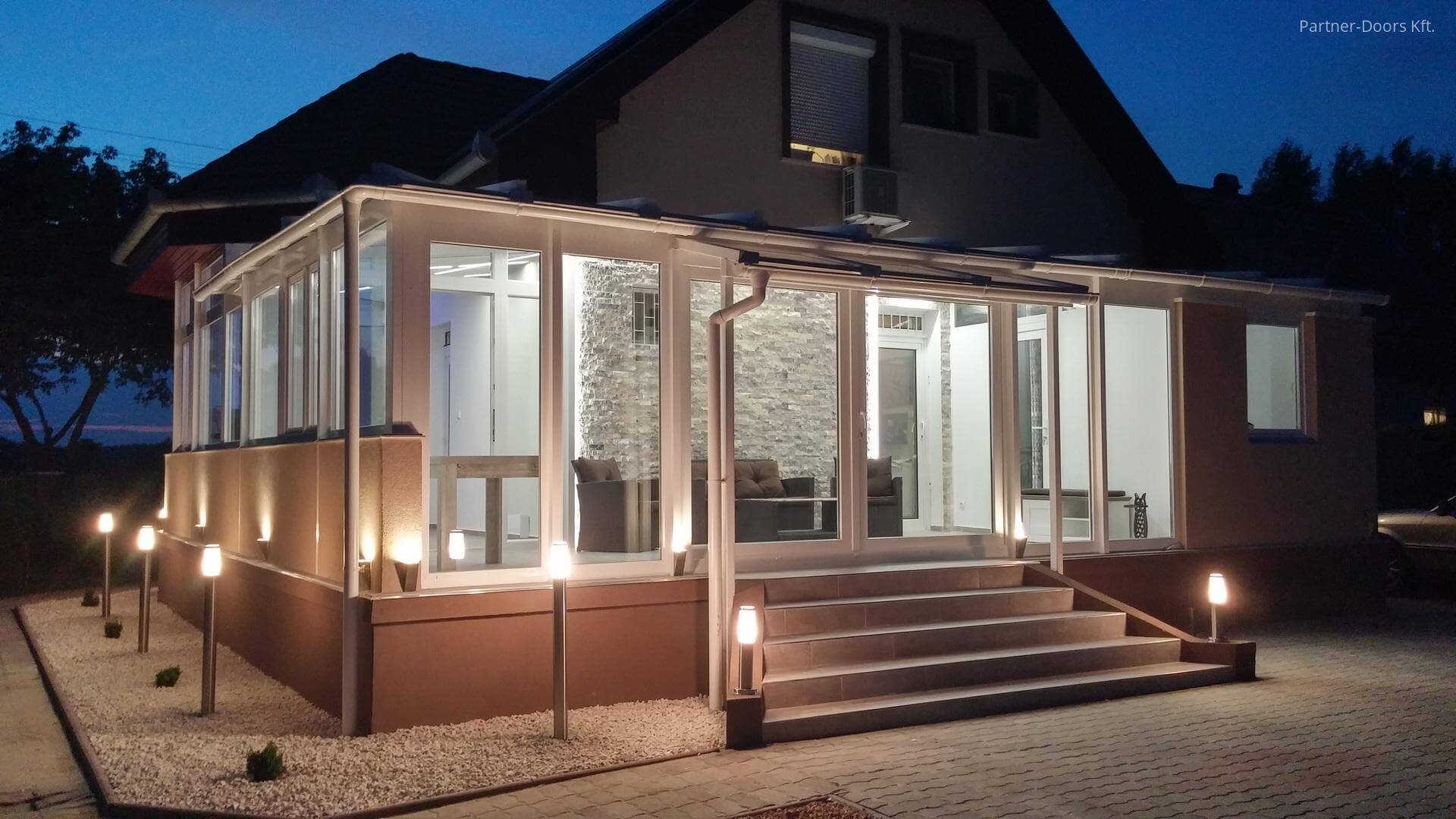 Illuminated glass house extension beside a home at dusk.