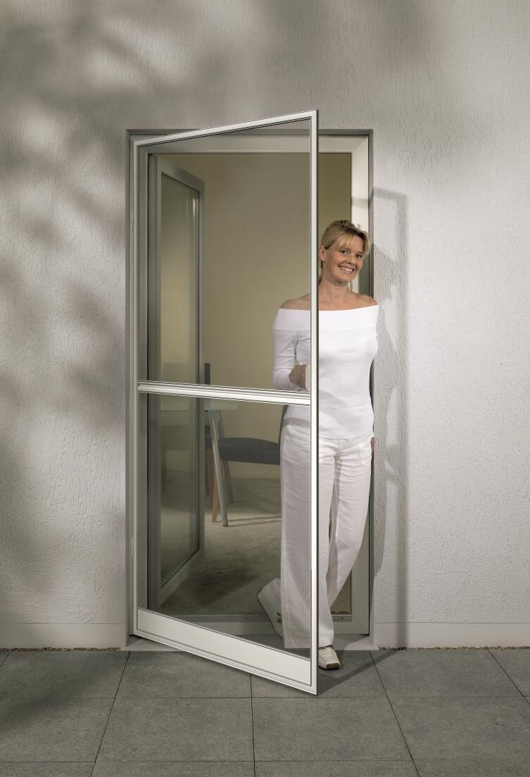 Smiling woman standing behind an open white-framed glass door.