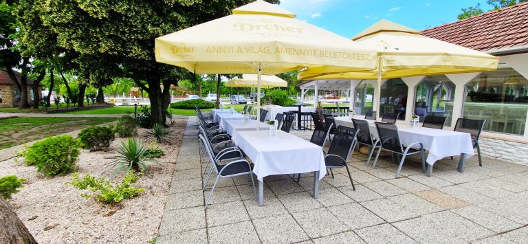 Kültéri terasz sárga napernyőkkel és hosszú terített asztalokkal.