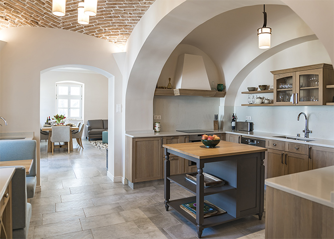 Arched opening frames a pale wood kitchen with a small central island.