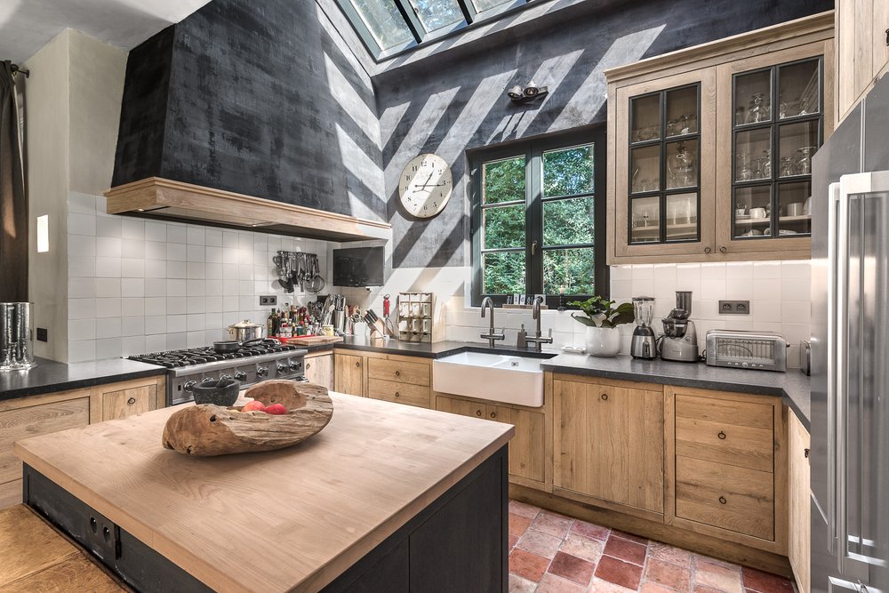 Dark cabinetry, large window and light wood island in a loft-like room.