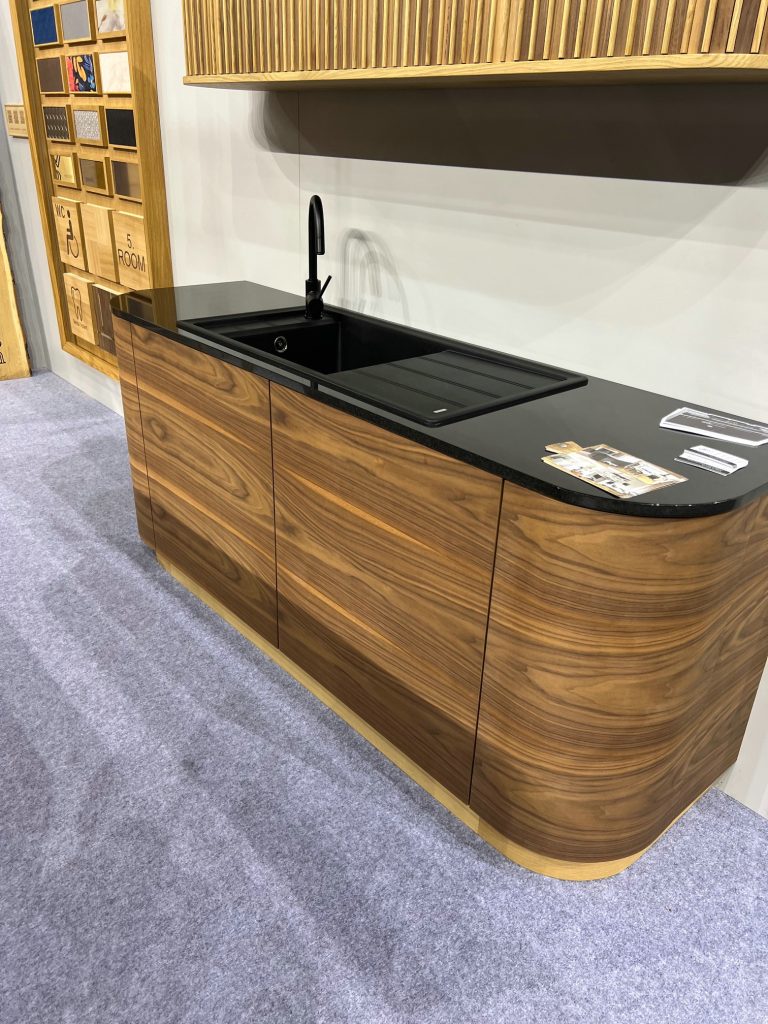 Curved wood kitchen base cabinet with black countertop and chair.