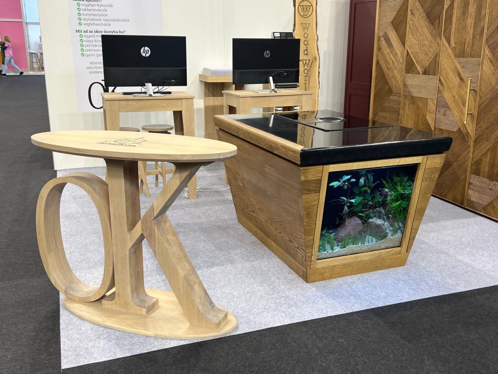Round wood table and compact island with screens in an exhibition hall.