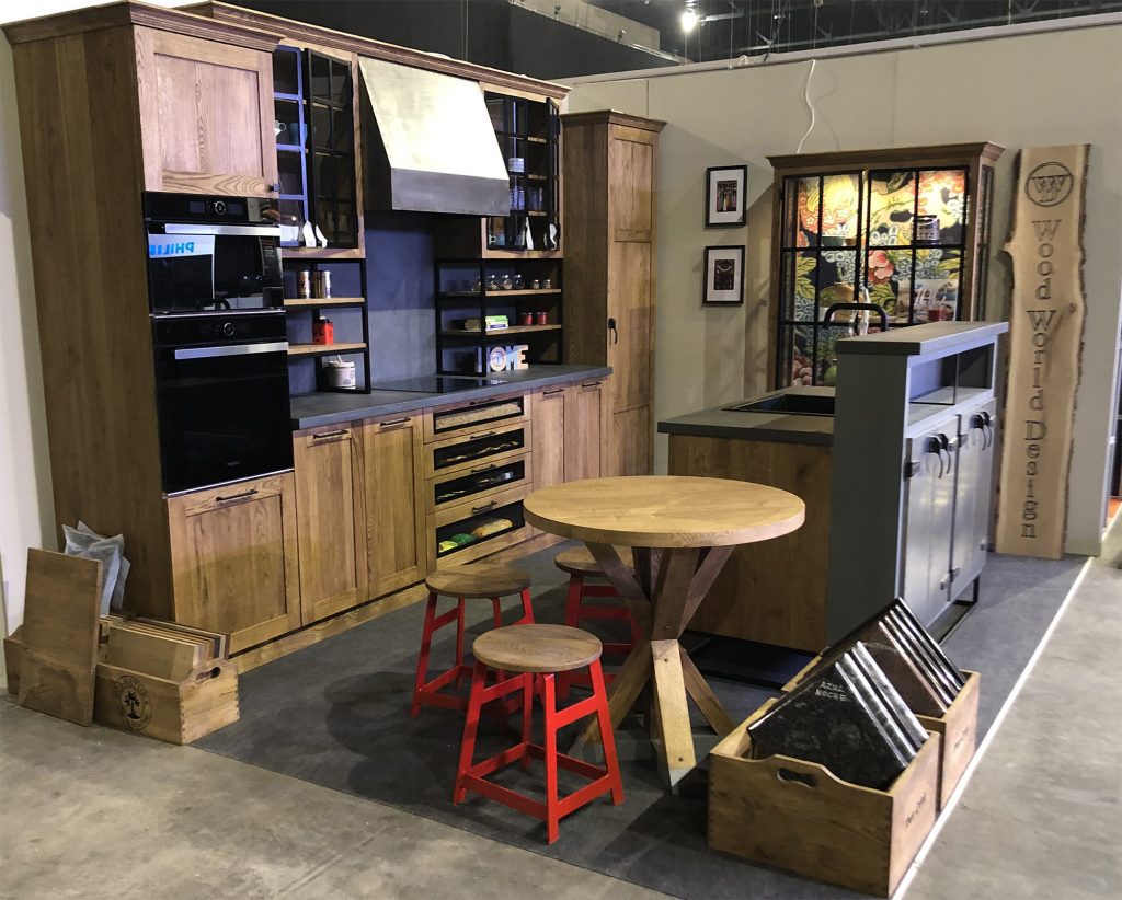 Wide exhibition stand with shelving, kitchen display and round tables.