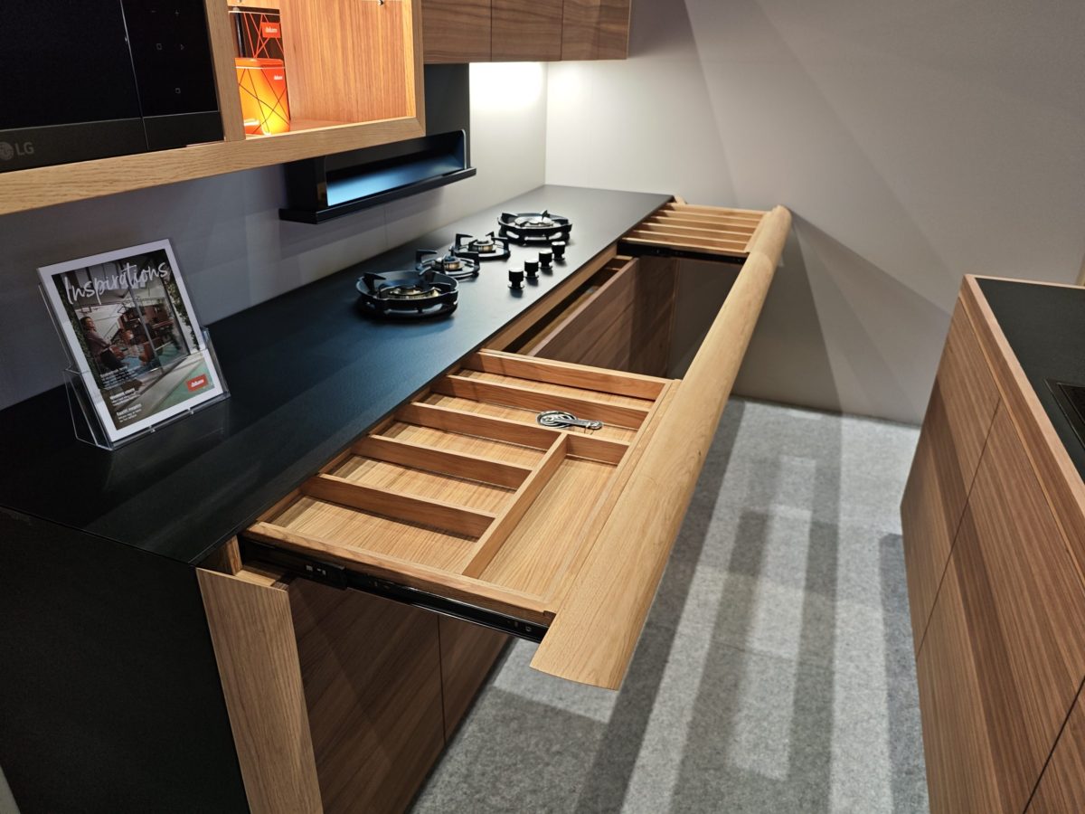 Wood cabinetry with open cutlery drawers beside a dark countertop.