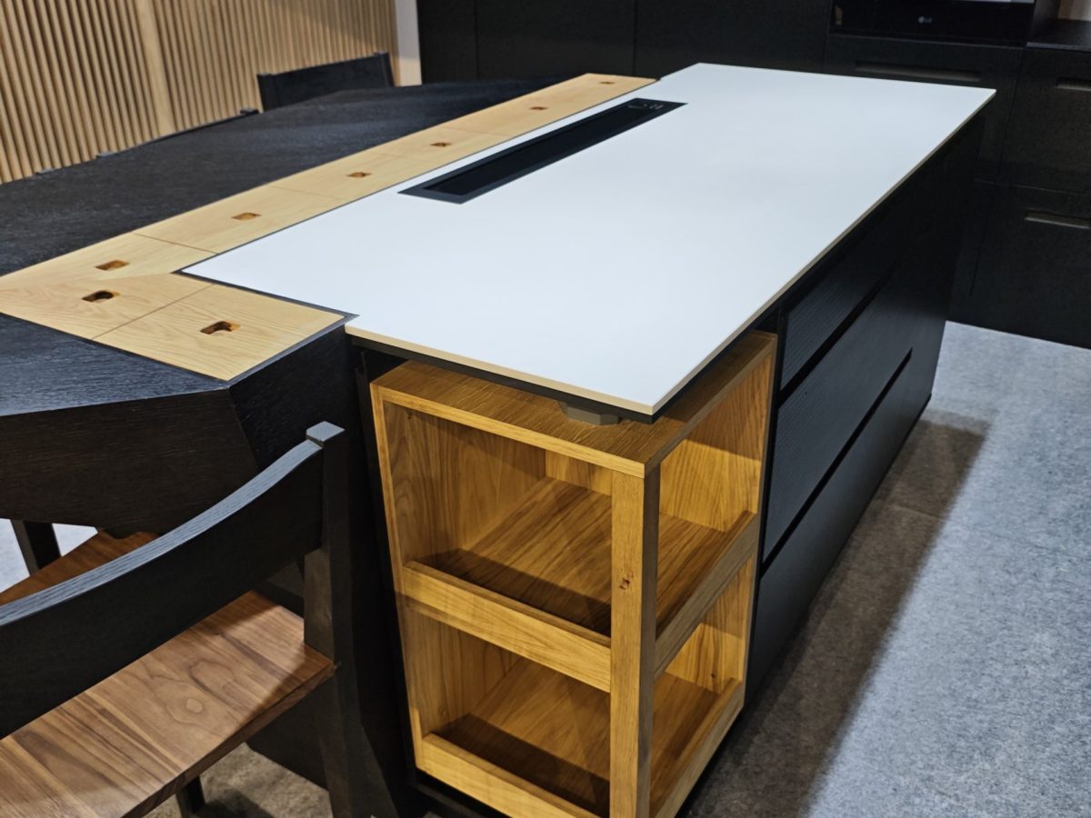 Wood island with white inset top and adjacent black cabinetry.