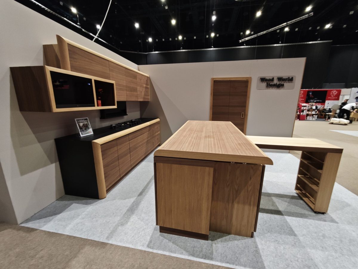 Wood table and wall shelving arranged in a dark exhibition booth.