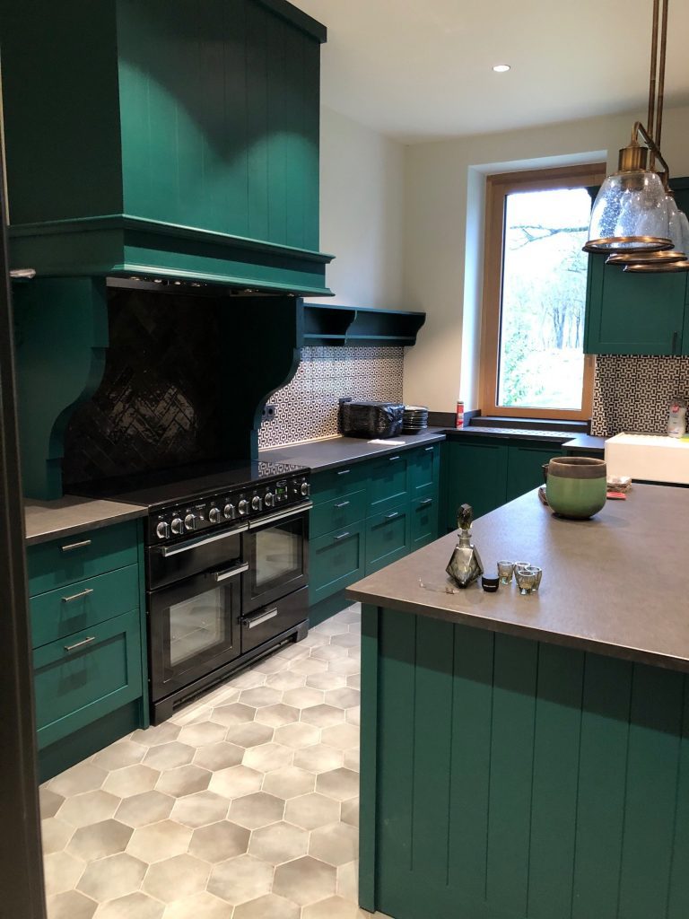 Vertical photo of deep green cabinets, wood worktop and black range.