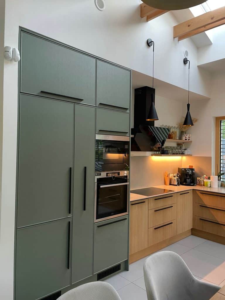 Green and wood cabinet run with built-in oven and dark countertop.