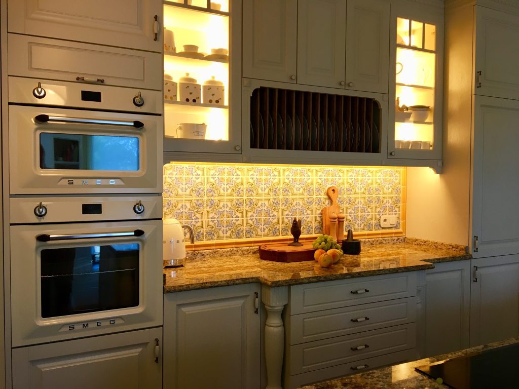 Warm illuminated wood kitchen wall with tall ovens and dark hood.