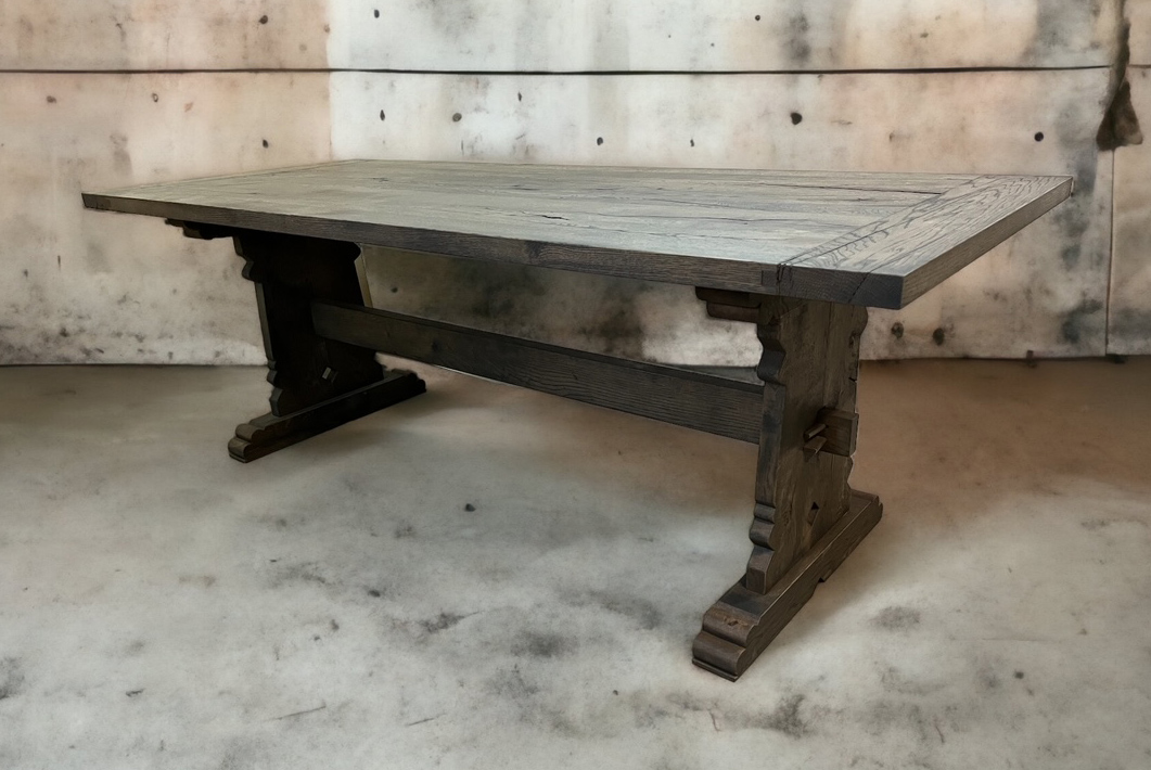 Long pale tabletop on dark x-shaped trestle legs in a concrete workshop.
