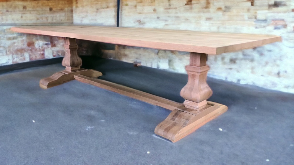 Wide pale tabletop on turned pedestal supports in a garage-like room.