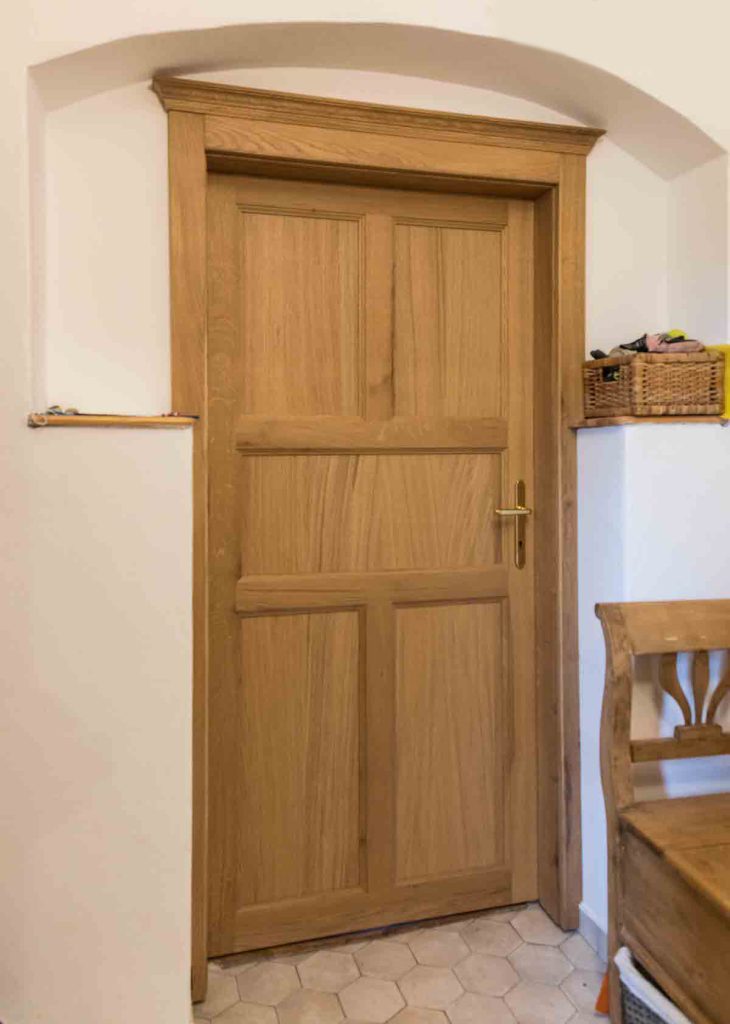 Closed warm wood door with raised panels under an arched frame.