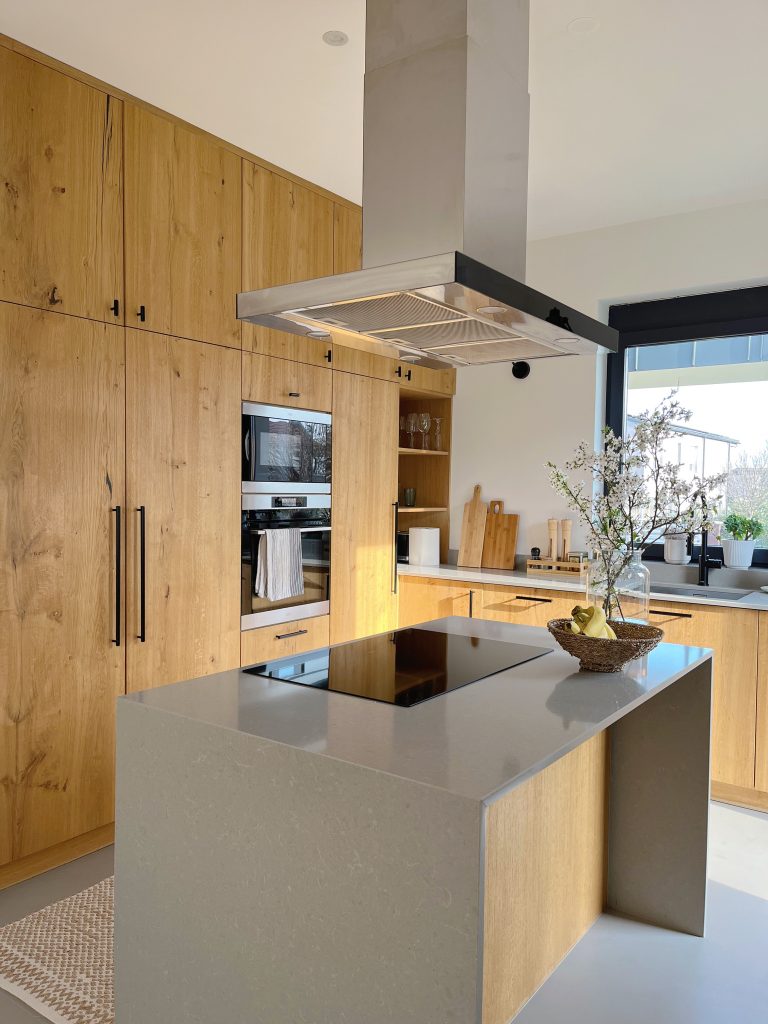 Vertical view of pale wood cabinets and a white island beside a dark hood.