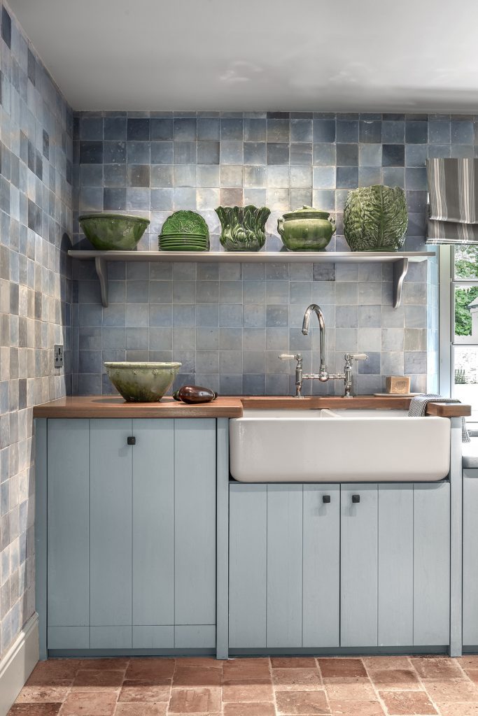 Vertical rustic kitchen with pale wood island, tiled backsplash and black range.