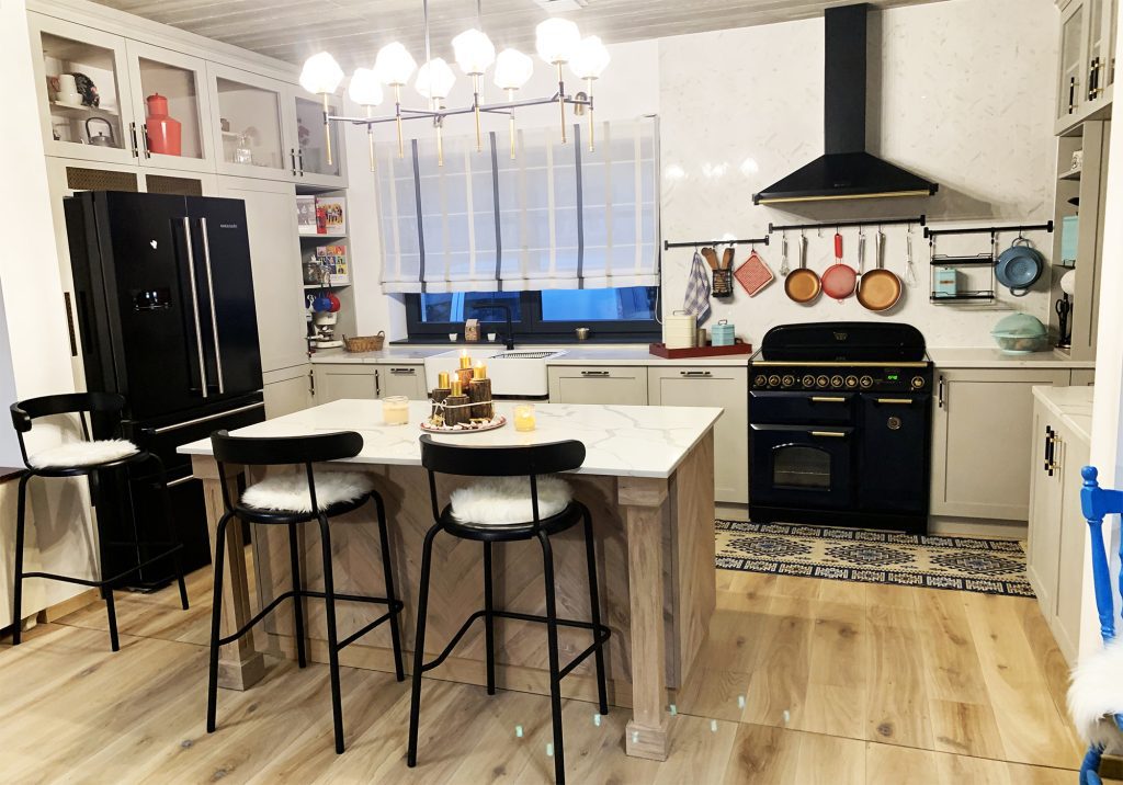 White kitchen with black refrigerator, range and stools around a peninsula.
