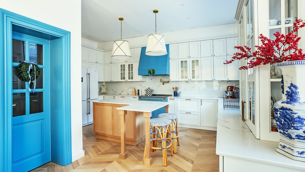 White cabinetry, bright blue door and small wood dining table by windows.