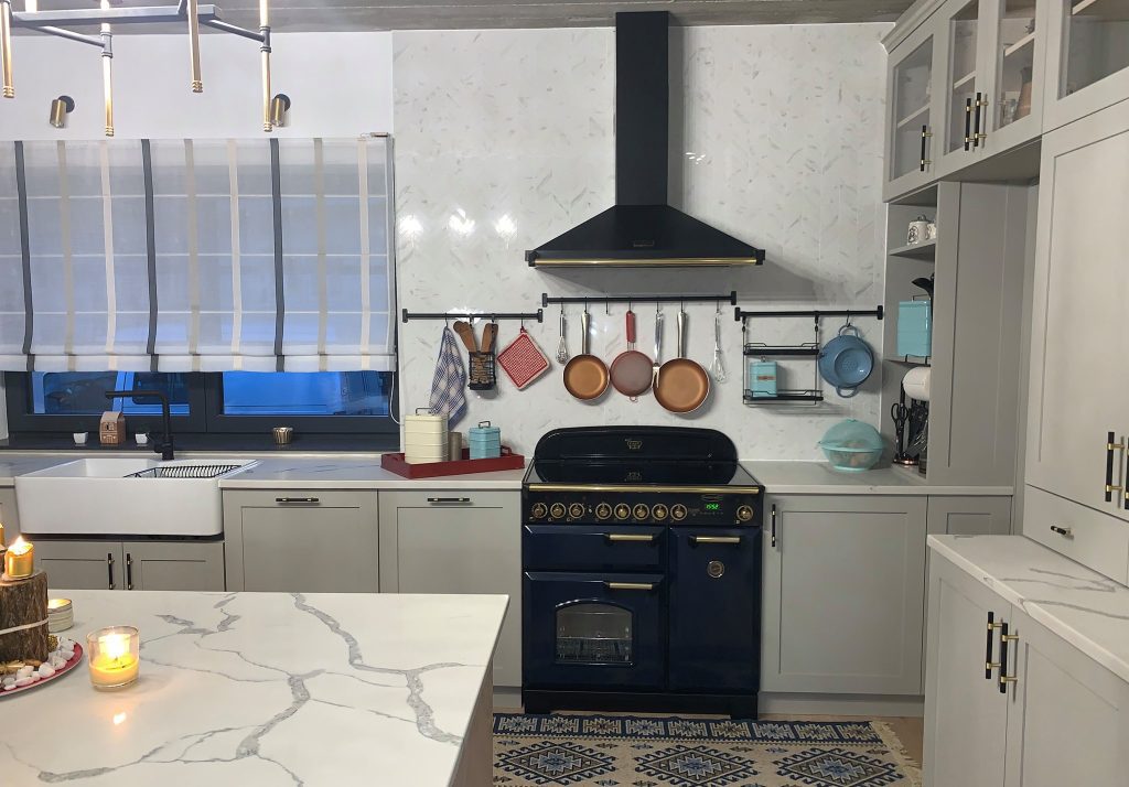 White paneled kitchen with black range, pale island and blue-shaded window.