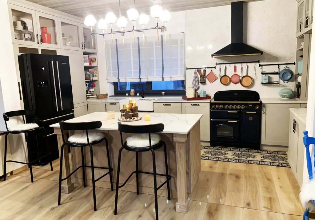 Bright white kitchen with island, black range and hanging cookware.