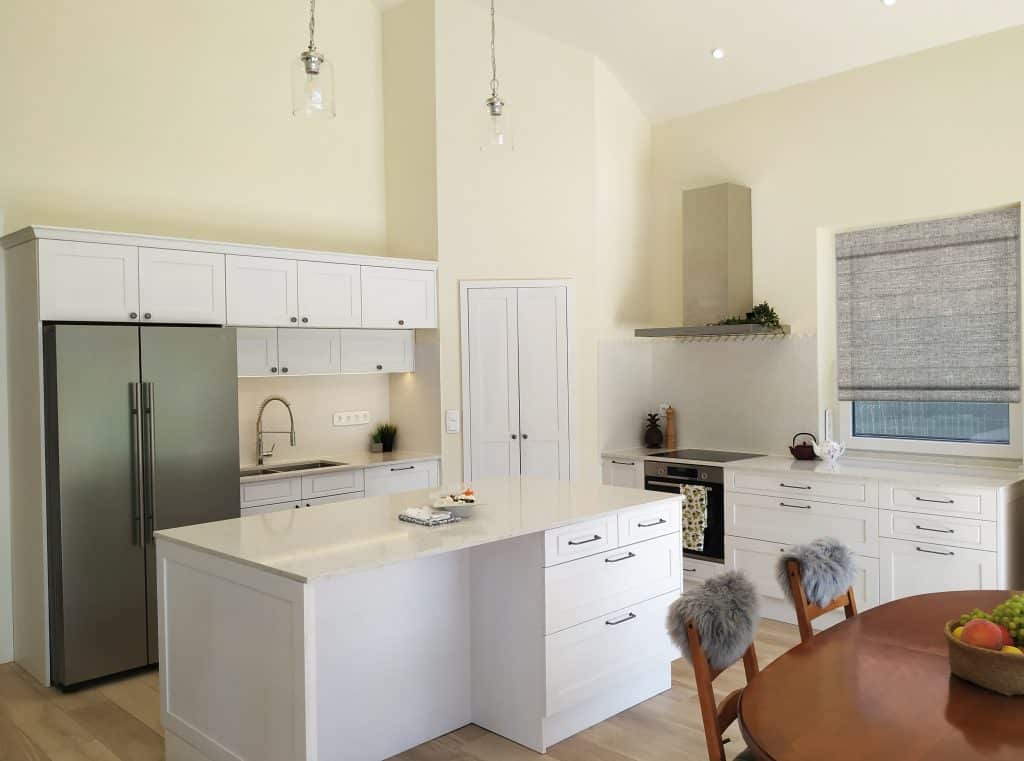 White minimalist kitchen with peninsula, stainless refrigerator and small seating area.