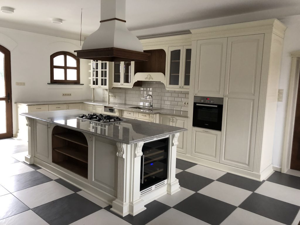 White paneled kitchen with checkered floor, island and black range hood.
